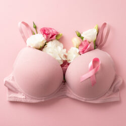 Promote breast cancer awareness. Top view of pink ribbon attached to bra filled with delicate eustoma flowers, symbolizing female well-being. Pastel pink backdrop, perfect for promo or advertisement