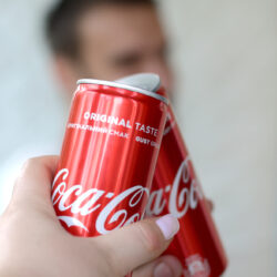 Happy young man raise Coca-Cola tin can with female friend in garage interior