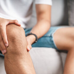 The man suffering from knee pain sitting on the couch holding an