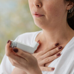 Allergic Asthma. A woman experiencing an asthmatic attack, holding an inhaler with medication to her face. Close up of hands. Blurry background
