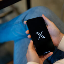 A female using X new twitter application on her iPhone14 while sitting in a coffee shop.